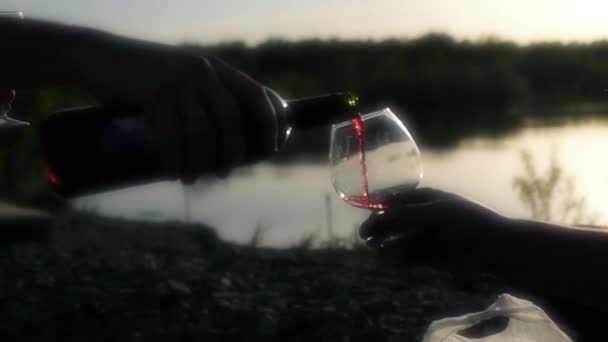 Despeje vinho tinto em um copo na natureza contra o pano de fundo do pôr do sol e do lago. câmara lenta — Vídeo de Stock