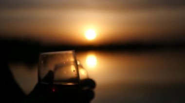 İki cam bardak ile arka planda çeşitli içecekler bir turuncu günbatımı su birbirleri ile tığ işi. Yavaş hareket tam hd 1080p