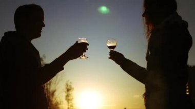 Sevgi dolu bir çift bardak kırmızı şarap ile kontrol edilir günbatımında ayakta. 4k.