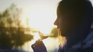 Genç güzel kız onun elinde kırmızı şarap ile yapar bir gurme lezzetli ferahlatıcı renkli arka plan günbatımı ve güneş parlamayı. HD. 1920 x 1080