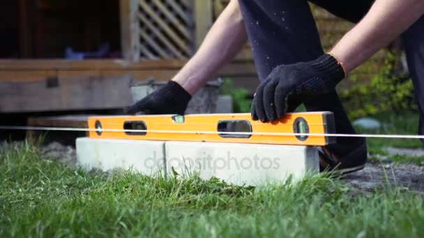 Legt der Arbeiter die Fliese in den Garten, legt sie mit Hilfe des horizontalen Werkzeugs in die Ebene. 4k. — Stockvideo