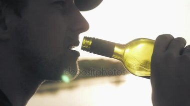 Genç adam bir gün batımı ve göl arka planda bir boğaz kırmızı şarap içecekler. Yakın çekim. Slowmotion. HD. 1920 x 1080