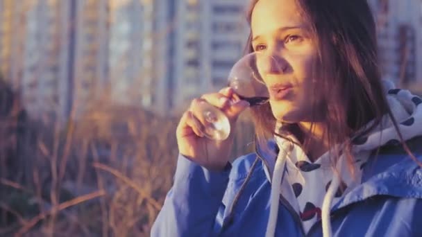 En flicka med glasögon vin i hennes händer, vilar i naturen och i solnedgången. 4 k. 840 x 2160 — Stockvideo