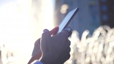 Bir çeşme bir görüntü ile şehirde bir arka plan üzerinde belgili tanımlık perde, saygısız bir dokunmatik telefon tutarak. Ağır çekim. HD, 1920 x 1080.