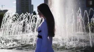 Hangi ferahlatıcı bir çeşme yakınındaki beyaz bir bluz yılında genç Kızıl saçlı kız modeli adım Parlatıcı ve güneş ışınlarının yansıtır. Ağır çekim. HD, 1920 x 1080.