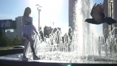 Güzel ince kız şehirde yürüyüş. Havuzun kenarı boyunca gider, geçmiş bir güvercin uçar. Ağır çekim. HD, 1920 x 1080.