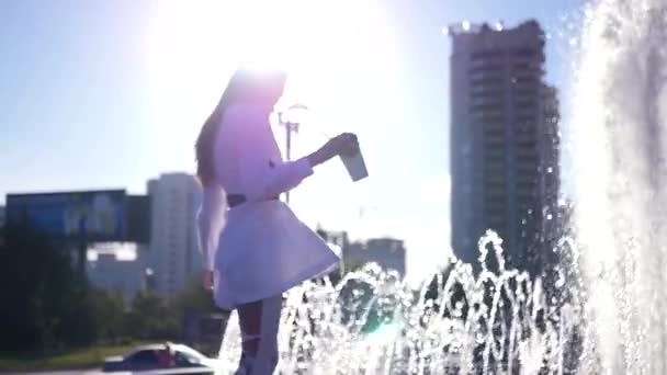 Una ragazza in piedi sul bordo di una fontana sta girando con una tazza di caffè in mano. SLOW MOTION. HD, 1920x1080 . — Video Stock