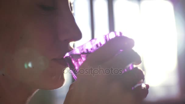 Молодая девушка пьет из красивого бокала из стекла, на заднем плане окна с эффективным объективом. Медленное движение. 1920x1080. макро — стоковое видео
