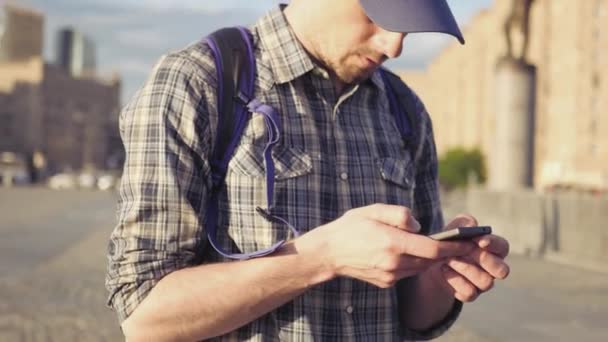 Ein junger Mann steht mitten in der Stadt und schreibt eine SMS am Telefon. 4k, 3840x2160. hd — Stockvideo