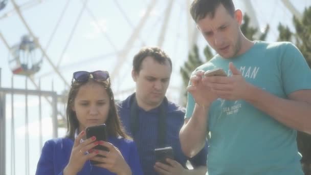 Група друзів, хлопці і дівчинка стоять з телефонами в руках і дивляться на них, вони вивчають карту. HD, 1920x1080. Повільний рух — стокове відео