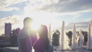 Sevgi dolu bir çift bir çeşme ve gün batımı arka plan üzerinde bir öpücük. HD, 1920 x 1080. Ağır çekim