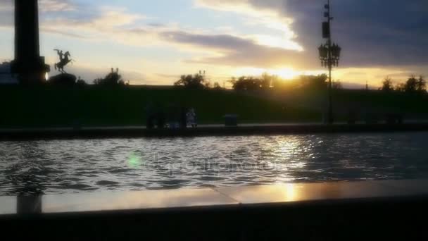 HD, 1920 x 1080. Slow motion. En ung flicka kör i en klänning på kanten av en fontän, mot en vacker solnedgång och reflektion i vattnet — Stockvideo