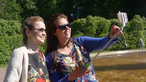 Deux jeunes copines faisant des photos au téléphone et selfie stick dans le parc vert. au ralenti. 1920x1080. hd complet — Video