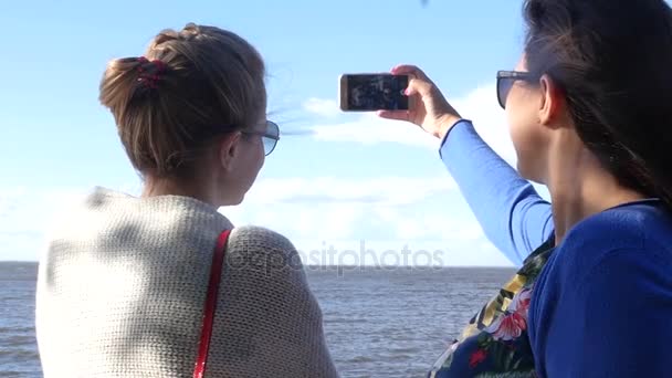 Dos amigos haciendo una foto en el teléfono de pie junto al mar en el paseo marítimo. cámara lenta. 1920x1080. hd completa . — Vídeos de Stock