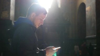 Bir adam bir telefon ile karanlık bir odada duruyor, bir ışık ışını pencereden düşer ve yansıtılır. ağır çekim. 1920 x 1080. hd tam