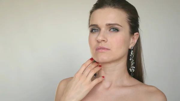 güzel genç model kendini yüzünü okşayarak beyaz bir arka plan üzerinde kamera için poz veriyor.