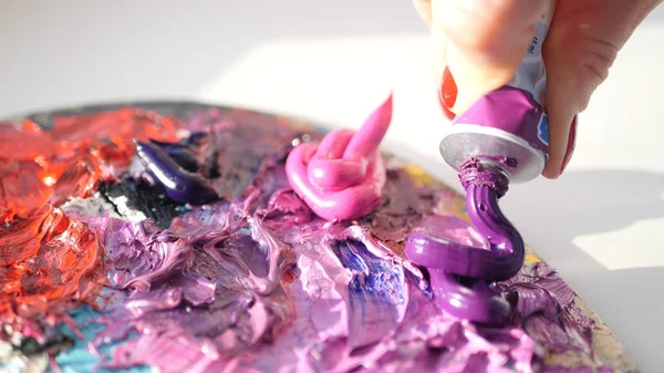Hd. Künstler quetscht sich aus der Röhre zur Palette lila öliger Farbe. lizenzfreie Stockfotos