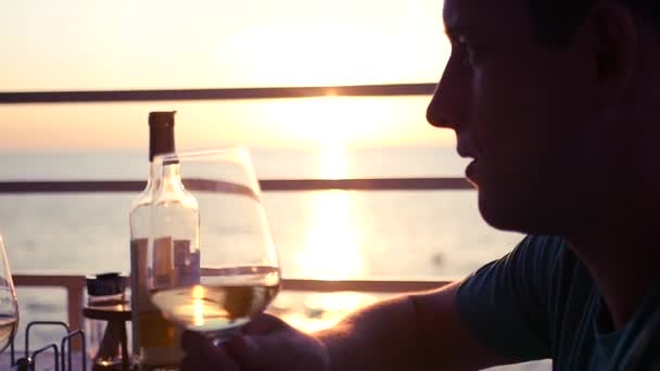 Genç çekici adam bir kadeh şarap deniz ve gün batımı bir kafede arka planı üzerinde konuşuyor. HD, 1920 x 1080. ağır çekim — Stok video