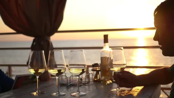 Twee vrienden zijn zittend in een restaurant aan het water in de buurt van de zee bij zonsondergang, drinken van wijn. HD, 1920 x 1080. Slow motion — Stockvideo