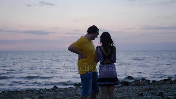 Jeune couple amoureux debout sur le bord de la mer contre le coucher du soleil, agitant les mains, salue joyeusement. En Haute Qualité, 1920 x 1080, au ralenti . — Video