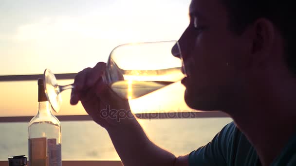 Un giovane sta bevendo vino bianco da un bicchiere in un bar al tramonto vicino al mare. HD, 1920x1080. rallentatore — Video Stock