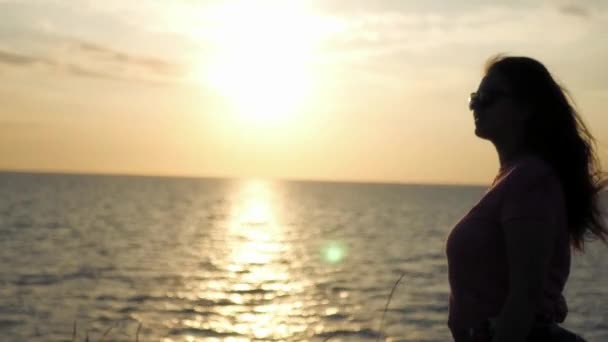 Μια νεαρή κοπέλα θαυμάζει το ηλιοβασίλεμα δίπλα στη θάλασσα, μια ελαφρά άνεμος φυσάει. 4k, 3840 x 2160. HD — Αρχείο Βίντεο