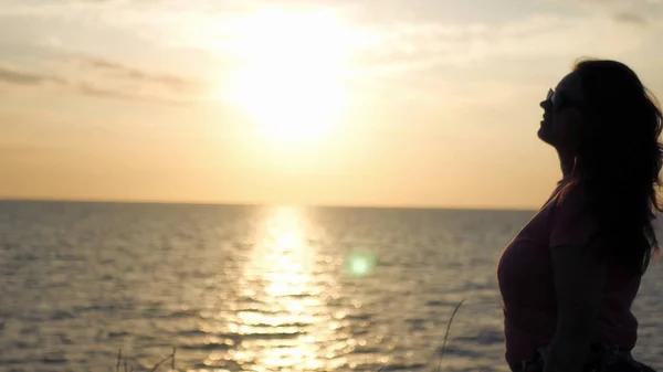 Genç bir kız güzel gün batımını deniz kenarında hayran, hafif bir Rüzgar uçurdu.