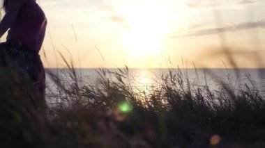 Mutlu kız yüksek çimen, arka planı güzel bir altın gün batımı ve deniz fırtınası ile araziyi çalışır. HD, 1920 x 1080, ağır çekim. HD, 1920 x 1080, ağır çekim.