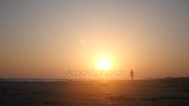 Yalnız kumlu bir plaj üzerinde deniz kenarında güzel bir gün batımı üzerinde yürüme. HD, 1920 x 1080. ağır çekim.