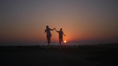 İki arkadaş el ele tutuşup batımında sahilde atlamak. HD, 1920 x 1080. ağır çekim.