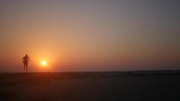 Läuft ein Mann wirbelnd am Strand entlang und hebt vor dem Hintergrund eines orangefarbenen Sonnenuntergangs die Hände. hd, 1920x1080. Zeitlupe. — Stockvideo
