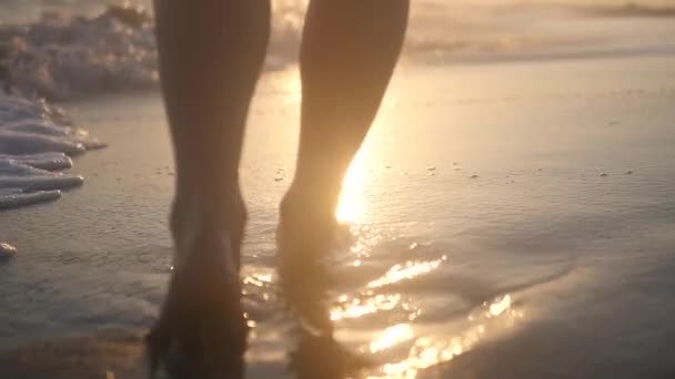 Bellissimi piedi femminili che camminano lungo la riva del mare con onde e spruzzi sullo sfondo di un bellissimo tramonto. HD, 1920x1080. rallentatore . — Video Stock