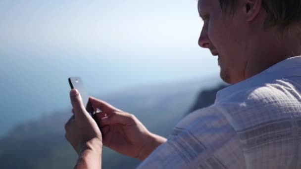 En man står på en klippa gör en foto panorama på telefonen. HD, 1920 x 1080. slowmotion. — Stockvideo