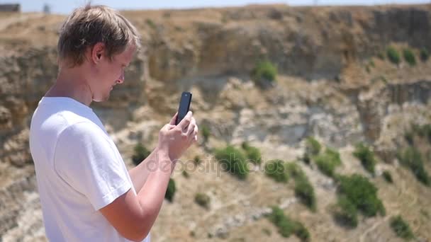 Egy férfi állt egy szikla úgy tesz egy képet a telefon. HD, 1920 x 1080. lassú mozgás. — Stock videók