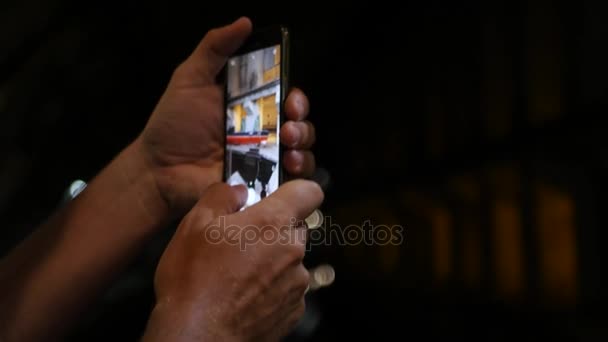 Un hombre sostiene un teléfono y fotografías en un cuarto oscuro, un primer plano. 3840x2160, 4K — Vídeos de Stock