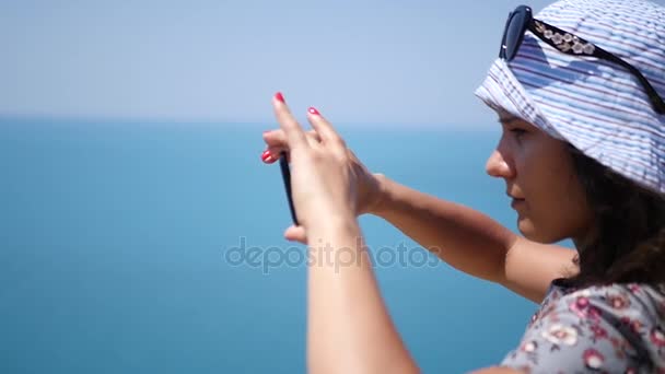 Beautiful young girl in a hat shoots a panorama of the sea on the phone. HD, 1920x1080. slow motion. — Stock Video