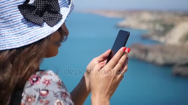 Uma menina em um belo chapéu azul fotografiruet mar azul do penhasco. HD, 1920x1080. câmara lenta . — Vídeo de Stock