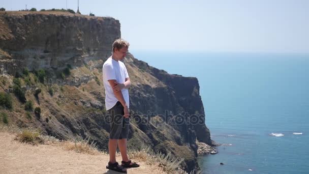 Чоловік стоїть на краю скелі, відпочиває і захоплюється чудовим видом. HD, 1920x1080. повільний рух . — стокове відео