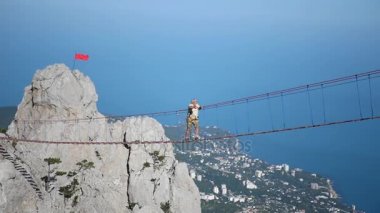 Güzel bir manzara karşı yüksek bir irtifada bir süspansiyon ip köprüde bir adam girer. HD, 1920 x 1080. ağır çekim.