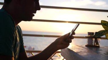 Genç adam bir telefonla günbatımında bir kafede. HD, 1920 x 1080. ağır çekim