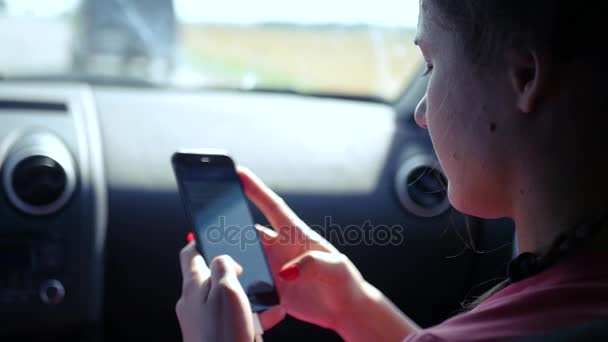 La chica pasajera está montando en el asiento delantero del coche, escribiendo un mensaje en el teléfono. HD, 1920x1080. cámara lenta — Vídeos de Stock