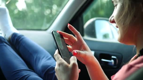 乘客的女孩坐在车子的前座，写入一条消息在手机上，把她的脚扔在面板上。高清，1920 x 1080。慢动作 — 图库视频影像