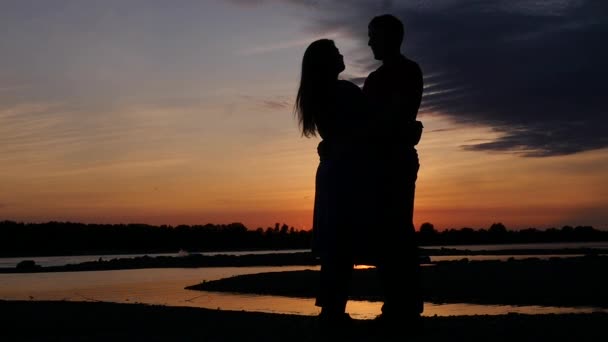 Egy férfi és egy nő van átölelve egy romantikus este a folyónál a naplemente. HD, 1920 x 1080. lassú mozgás. — Stock videók