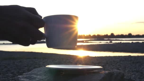 Campt bei Sonnenuntergang am Fluss und stellt eine Tasse heißen Tee auf einen Stein und eine Untertasse. Zeitlupe, 1920x1080, hd — Stockvideo