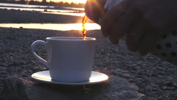 Gießen Sie bei Sonnenuntergang einen köstlichen heißen Tee oder Kaffee am Fluss in eine weiße Tasse aus einer Thermosflasche. Zeitlupe, 1920x1080, hd — Stockvideo