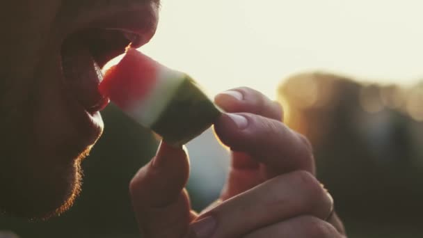 Un hombre está comiendo una deliciosa sandía roja madura, un fondo borroso. 4k, 3840x2160. HD — Vídeo de stock