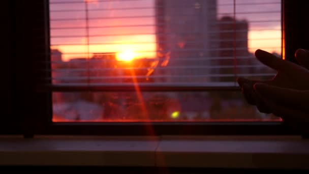 Un hombre y una mujer se estiran uno hacia el otro, tomados de la mano en la ventana contra el telón de fondo de la ciudad y una hermosa puesta de sol. HD, 1920x1080. cámara lenta . — Vídeos de Stock
