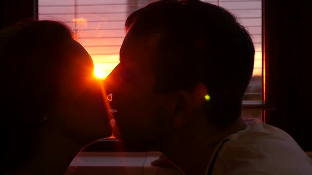 Um homem e uma mulher apaixonados beijam-se em casa contra a janela e num lindo pôr-do-sol ardente. câmara lenta, HD, 1920x1080 — Vídeo de Stock
