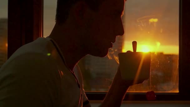 A young man rests in the evening at sunset and drinks hot tea by the window. HD, 1920x1080. slow motion. — Stock Video