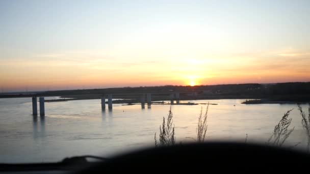 Hermosa puesta de sol sobre el río y el puente con vista desde el coche y el timón. cámara lenta, 1920x1080, full hd — Vídeos de Stock